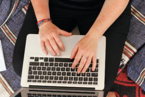 A woman’s hands typing on a laptop on her lap.